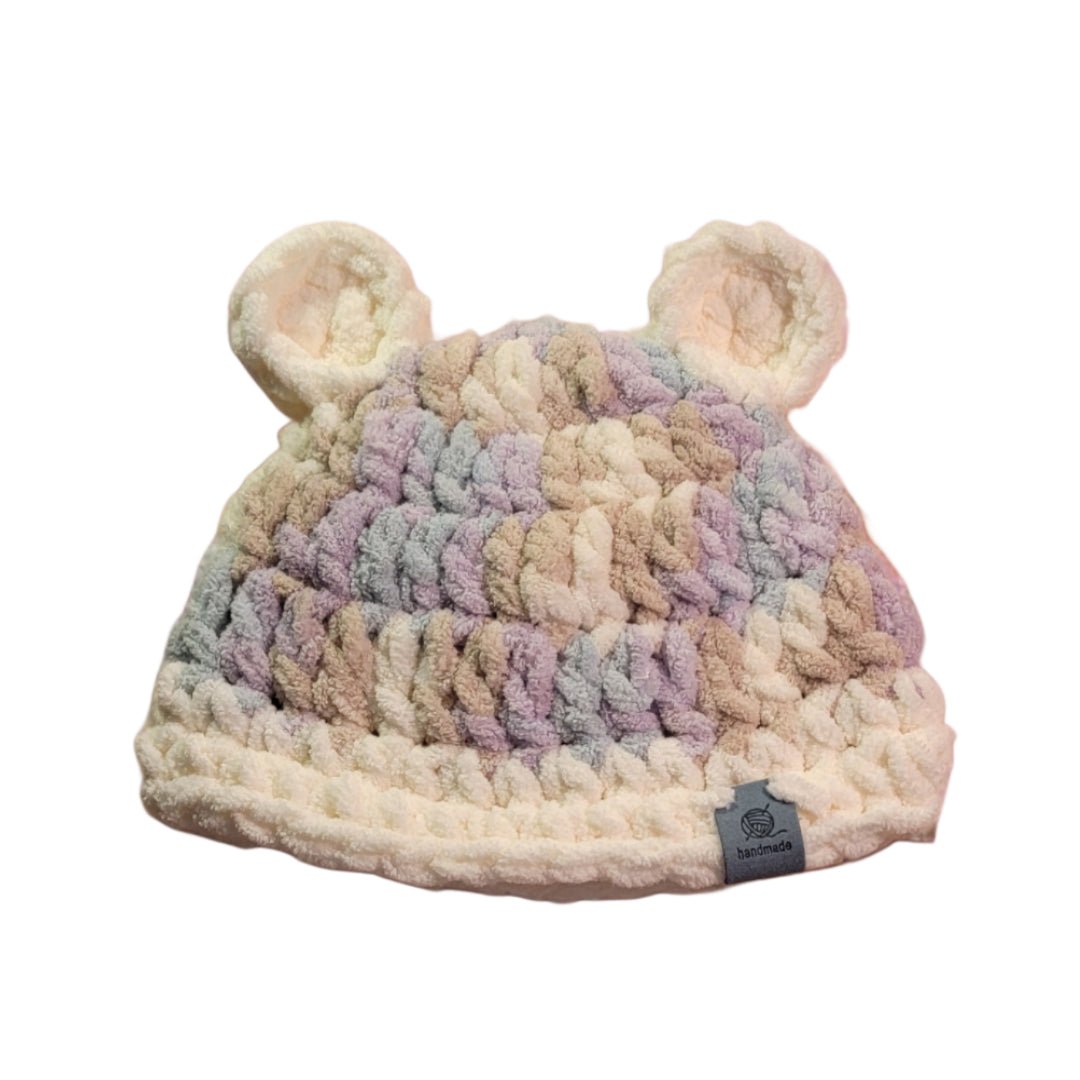 Baby beanie with teddy bear ears. Crocheted in a lavender camo color and vintage white with a blue product tag attached to the bottom rim.